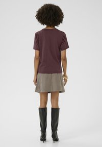 Bordeaux katoenen t-shirt, korte mouwen; bruine geruite rok; kniehoge zwarte haklaarzen. Glad textuur, moderne pasvorm. Eenvoudige, strakke lijnen.