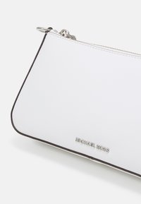 Bijela kožna torbica trokutastog oblika, sa srebrnim detaljima, zatvaranjem na patentni zatvarač, i crnim obrubom s urezanim "Michael Kors" logotipom.