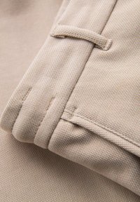 Tejido beige con un tejido texturizado y costuras limpias. El detalle del puño enrollado muestra un acabado limpio y una costura de acento oculta en el borde.