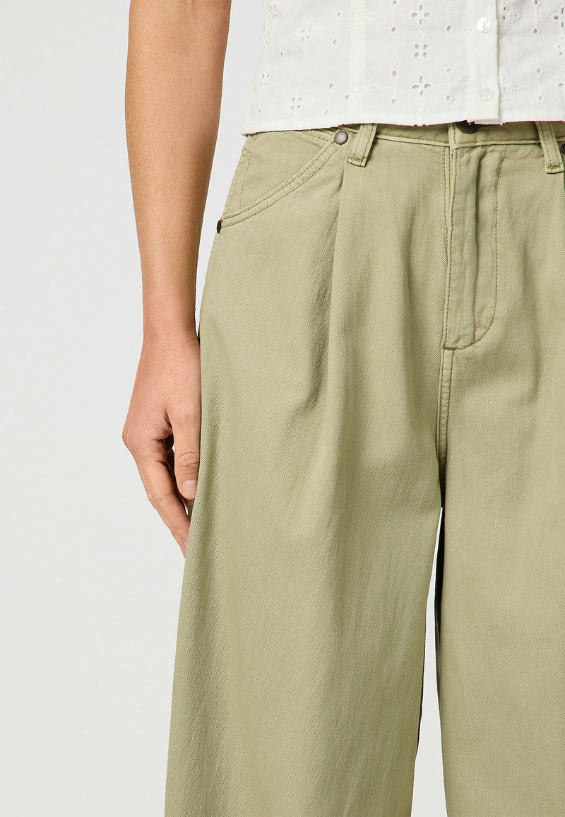 Pantalons plissés verts clairs en coton, dotés de poches latérales, de fermeture à bouton et d'une coupe légèrement ample.