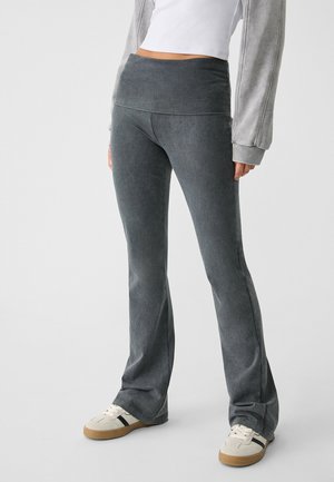 Person wearing high-waisted, dark grey flare pants, white crop top, grey long-sleeve jacket, and white sneakers with black stripes.