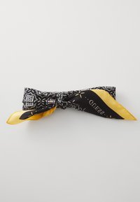 Écharpe à motif noir et jaune avec une texture en soie. Présente des motifs complexes, un nœud noué et une étiquette de logo sur un côté.