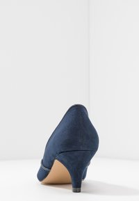Chaussure à talon haut en daim bleu marine avec un bout pointu, un talon court et une texture lisse ; dotée d'une couture sur le dessus.