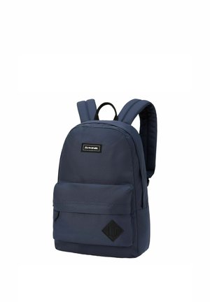 Zaino Dakine blu navy con spallacci imbottiti, tasca frontale con cerniera e toppa a forma di diamante nera sulla parte anteriore inferiore destra.