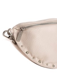 Miękka beżowa skórzana torba w kształcie półksiężyca, z zapięciem na zamek i srebrnymi okuciami. Dekoracyjne srebrne ćwieki wzdłuż krawędzi.