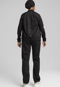 Melnas sporta treniņtērps ar bomber stila augšu un sašaurinātām biksēm. Gluda tekstūra, ribotas aproces un apakšmala. Neformāls dizains, minimālas detaļas.