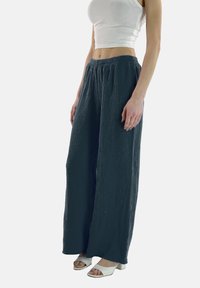 Wijde broek gemaakt van een gestructureerde donkere stof met een elastische tailleband, gecombineerd met witte open-hak schoenen en een aansluitend wit topje.