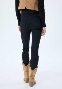 Vaqueros skinny negros de cintura alta, con dos bolsillos traseros. Combinados con botas de cowboy de color marrón claro, con un diseño de costura y un tacón resistente.