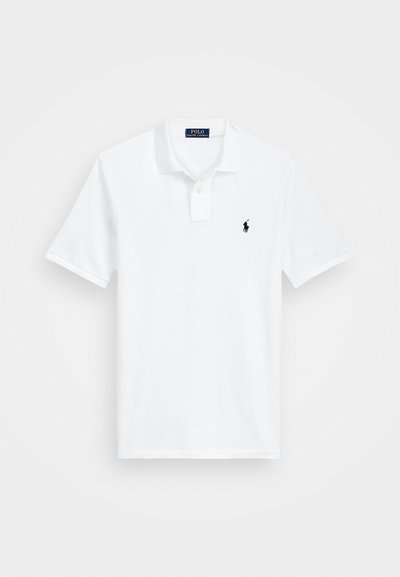 Hvit polo skjorte laget av bomull, med en tre-knapps placket, korte ermer og en marineblå logo brodert på venstre bryst.