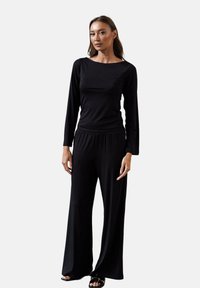 Czarny longsleeve z dekoltem typu boat, zestawiony z szerokimi czarnymi spodniami. Materiał jest gładki i miękki, a fason luźny. Prosty design.