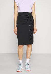 Černá tužková sukně s texturovaným bočním volánem, obsahující sedm knoflíků na přední straně. Materiál je hladký s těsným designem.