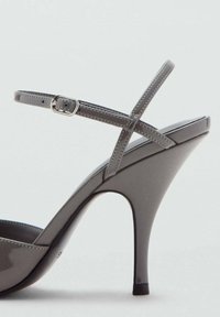 Szare lakierowane sandały na wysokim obcasie o eleganckim designie, z krzyżującymi się paskami, zapięciem na kostkę i wyraźnie zwężanym obcasem.