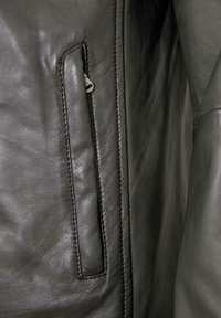 Schwarze Lederjacke mit einem Reißverschlussfach, strukturiertem Oberflächenbild und sichtbaren Nähten entlang der Kanten. Glattes, geschmeidiges Material.