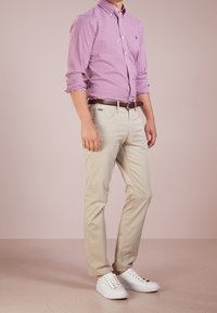 Dopasowana, różowa koszula w kratę zapinana na guziki, beżowe chinosy, brązowy pasek i białe trampki. Gładki materiał o przemyślanej konstrukcji.