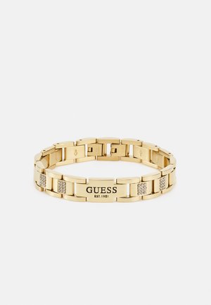 Pulseira em tom de ouro com elos interligados, marcada com "GUESS EST.1981" e acentuada com pedras brilhantes entre alguns elos.