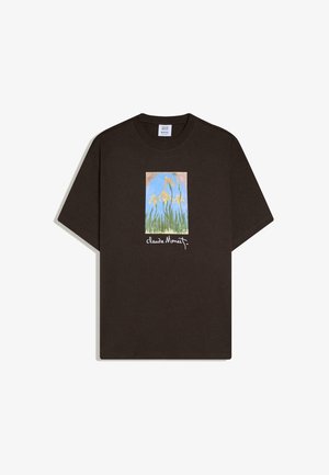 Schwarzes T-Shirt mit kurzen Ärmeln und einem rechteckigen Druck gelber Schwertlilien vor blauem Himmel, darunter steht "Claude Monet" geschrieben.