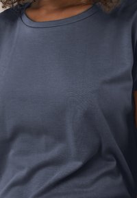 Detailní záběr na osobu v námořnickou modrou tričko, ukazující texturu a výstřih, s zachycenými jemnými sklady látky.