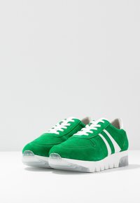 Sneakers verde in suede con strisce bianche, pannelli in mesh testurizzati e suola in gomma trasparente. Presentano lacci bianchi e colletto imbottito.