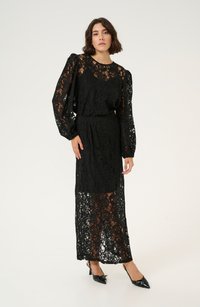 Black lace dress with long, puffed sleeves, floral patterns, fitted waist, and a flowy skirt. Paired with shiny black pointed heels.