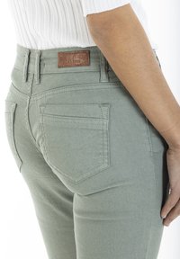 Pantalons taille haute vert clair avec une texture lisse, dotés de deux poches arrière et d'une étiquette en cuir marron avec "RICA LEVIS 1978".