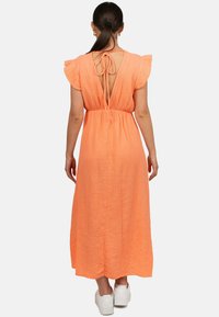 Lungo vestito arancione senza maniche realizzato in tessuto texturizzato, con un profondo scollo a V sul retro, maniche voluminose e chiusura con lacci. Indossato con sneaker bianche.
