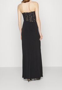 Svart strapless aftonklänning med en figurnära silhuett, spetslivstycke och flödande material. Knälång kjol med subtil textur och detalj.