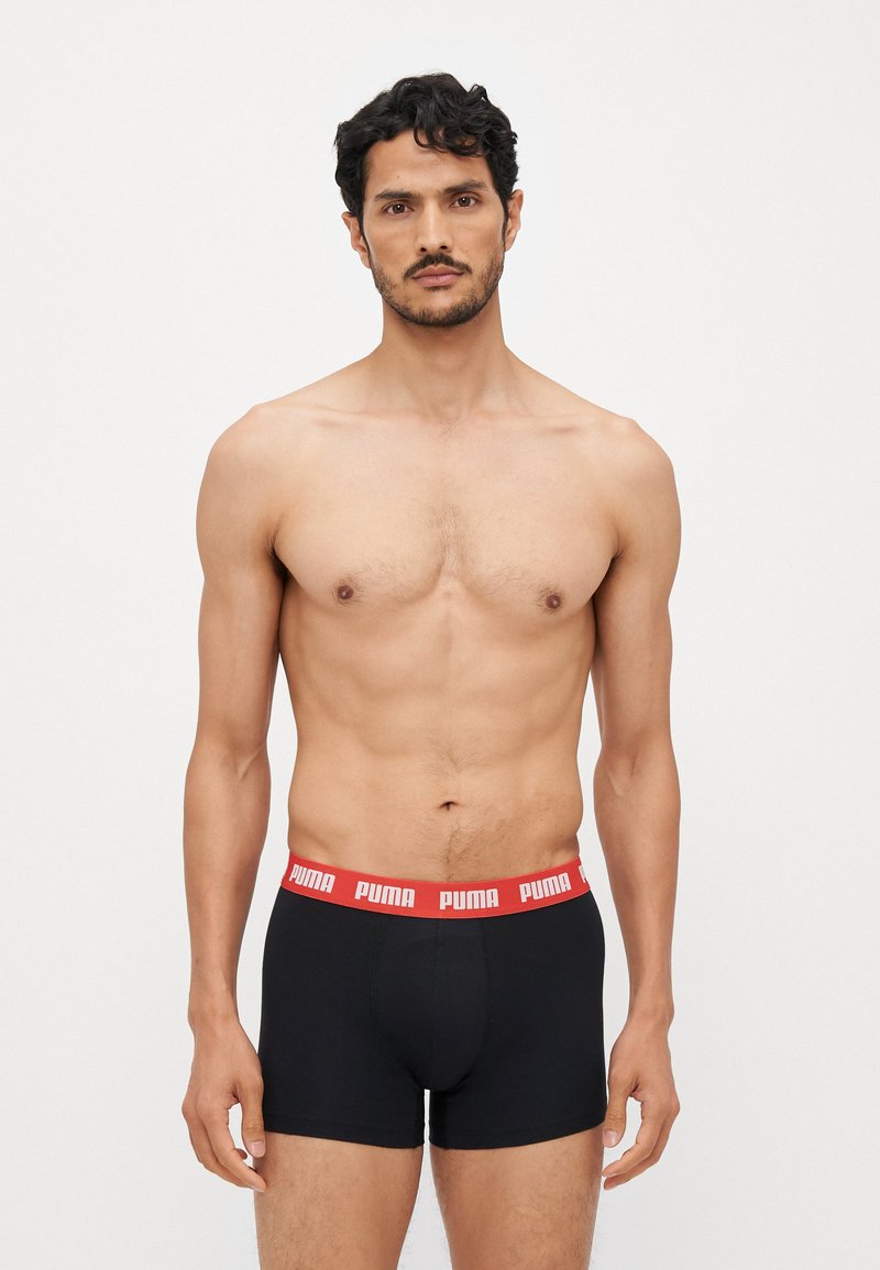 Schwarze Boxershorts mit einem breiten roten Puma-Bund. Der Stoff wirkt glatt und dehnbar, entworfen für Komfort und Passform. Das Modell steht aufrecht.