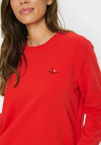 Roter Pullover aus weichem Material mit rundem Halsausschnitt und langen Ärmeln, verziert mit schwarzem gesticktem Text "love" und einem kleinen Herzdetail.