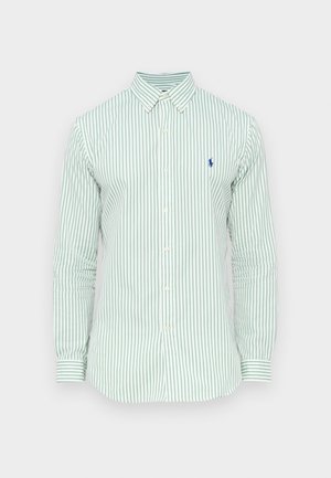 Šviesiai žalia dryžuota marškiniai su ilgomis rankovėmis, sagomis užsegamu apykakliu ir mažyčiu mėlynu logotipu ant krūtinės. Medvilnės audinys su lygiu paviršiumi.