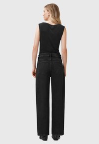 Zwarte mouwloze top gecombineerd met hoge taille, wijdvallende zwarte jeans. Opvallende details zijn achterzakken en gestifte zwarte schoenen.