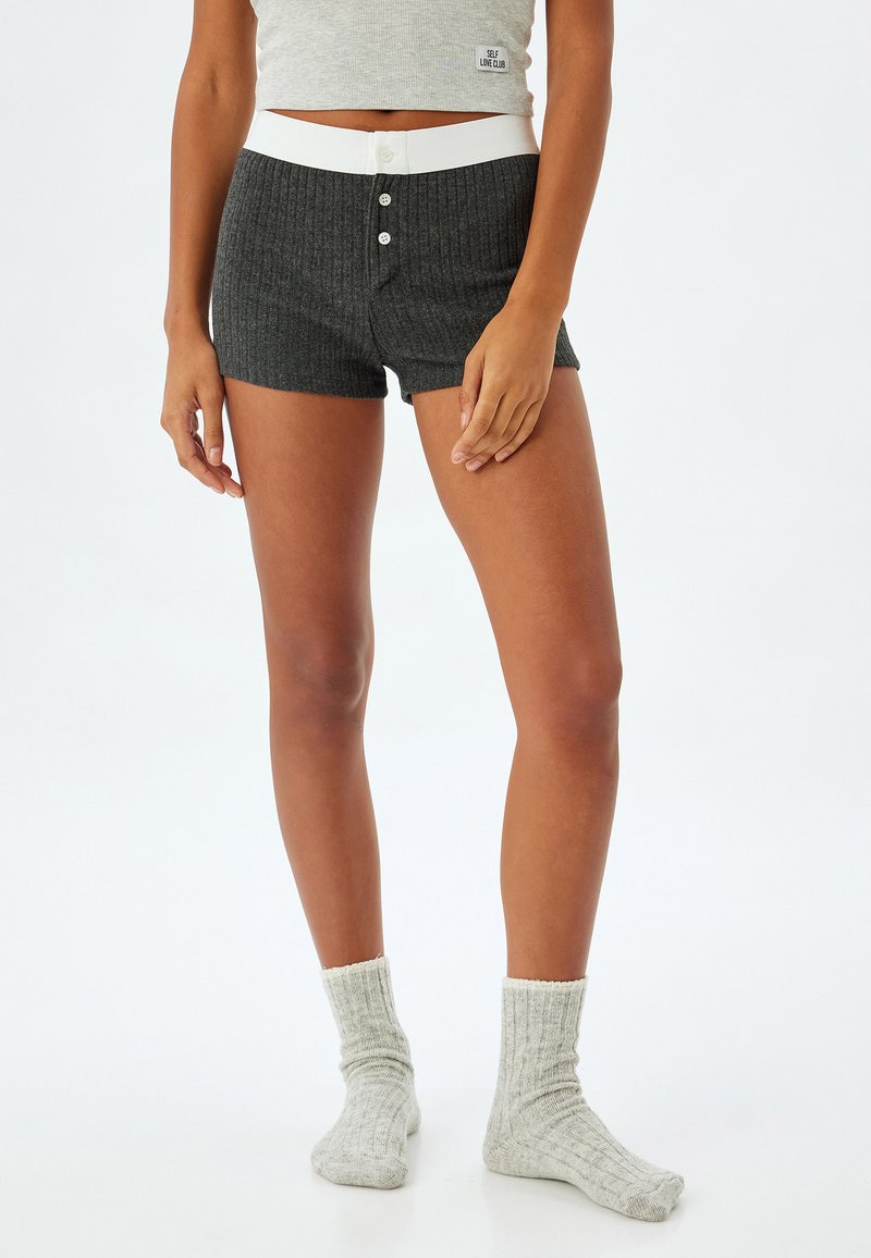 Grijze geribbelde shorts met een witte elastische tailleband en drie knopen. Gecombineerd met lichtgrijze gestructureerde gebreide sokken. Minimalistisch ontwerp.
