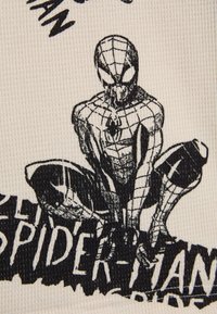 Illustration en noir et blanc de Spider-Man sur un tissu crème, présentant une surface texturée à côtes et le nom "Spider-Man" en lettres grasses.