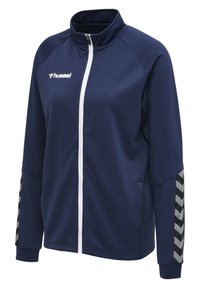 Marinblå zip-up jacka i texturerat tyg, med en vit dragkedja och randiga detaljer i grått och svart på ärmarna.