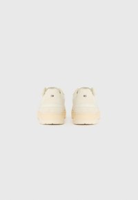 Cream-colored suede sneakers with a textured finish and a rubber sole. Features a small logo detail on the back.