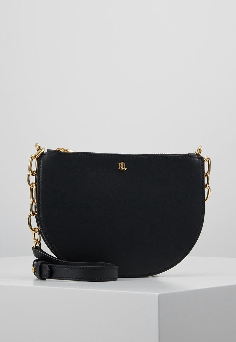 Sac en cuir noir à bandoulière avec une forme incurvée, chaîne dorée, et détail de logo. Il possède une fermeture zippée et une bandoulière amovible.