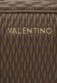 Ruda odinė rankinė su siuvinėta raštu. Yra aukso spalvos ženklas su "VALENTINO" didžiosiomis raidėmis, akcentuota siuvinėta tekstūra ir lygi paviršius.