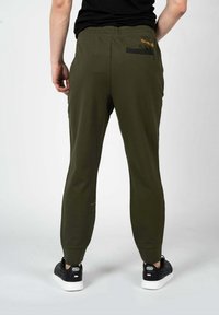 Olivengrønne joggerbukser lavet af blødt stof, med en slim fit, elastisk talje og en sort lynlåslomme på bagsiden.