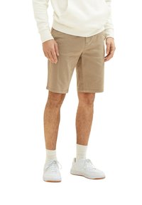 Beige Baumwollshorts mit Seitentaschen, flachem Bund und umgeschlagenem Saum. Kombiniert mit weißen Sneakers und cremefarbenen Socken.
