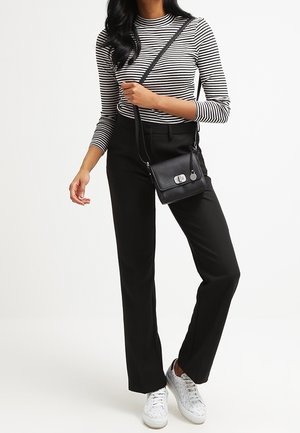 Zwarte crossbodytas met een gestructureerde afwerking, zilveren hardware en verstelbare schouderriem. Het model draagt een gestreept shirt en zwarte broek.