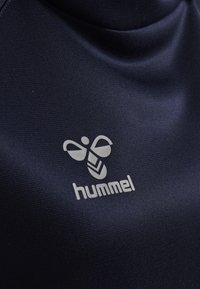 Maglia sportiva navy con un tessuto liscio e strutturato. Presenta un logo grigio chiaro di un'ape stilizzata e il nome del marchio "hummel" in basso.