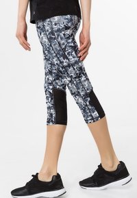 Leggings Capri en noir, blanc et nuances de gris avec des motifs géométriques. Présente des panneaux latéraux noirs et des coutures contrastantes.