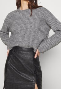 Szary sweter z dzianiny o okrągłym dekolcie i prążkowanej fakturze, w połączeniu z czarną spódnicą o fasonie ołówkowym z faux skóry, z bocznym rozcięciem.