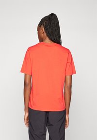 T-shirt en coton rouge avec des manches courtes, un col rond et un dos uni. Texture lisse et design décontracté.