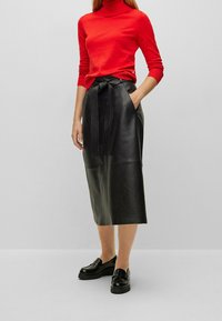 Svart läder midi-kjol med ett texturerat bälte, i kombination med en åtsittande röd polo-tröja. Skorna inkluderar svarta loafers.