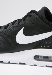 Svart idrottssko med en texturerad ovandel, vit Nike swoosh och en synlig luftenhet i hälen, med en vit yttersula och svarta detaljer.