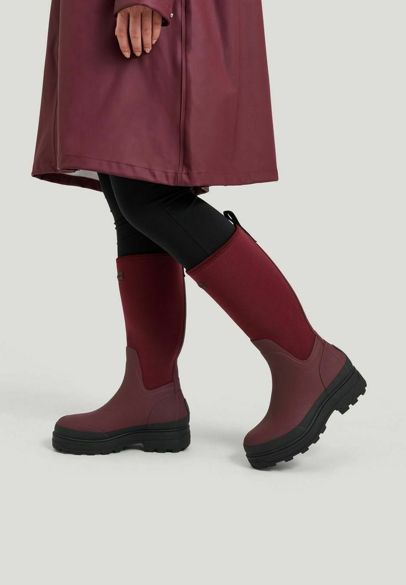 Gummistövlar i vinröd med en texturerad yta och svart gummisula. Har en snug passform vid vaden med en slät design och subtila detaljer.