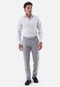 Weißes Hemd mit langen Ärmeln, kombiniert mit grauen, maßgeschneiderten Hosen. Glatter Stoff, schmaler Schnitt und seitliche Taschen prägen das Design.