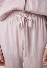 Pigiama rosa chiaro con strisce verticali verdi e bianche. Presenta una cintura elastica con un laccio in satin. Tessuto dalla consistenza morbida.