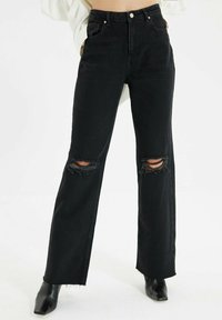 Jeans neri a vita alta realizzati in denim, con design a gamba dritta, dettagli di strappi sulle ginocchia e orlo grezzo.
