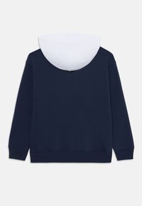 Felpa blu navy con una foderatura bianca sul cappuccio, realizzata in tessuto morbido; presenta maniche lunghe e una vita e polsini a coste.